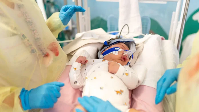 A photo of an infant being treated for bronchiolitis, lying in a hospital bed wearing a nasal cannula.